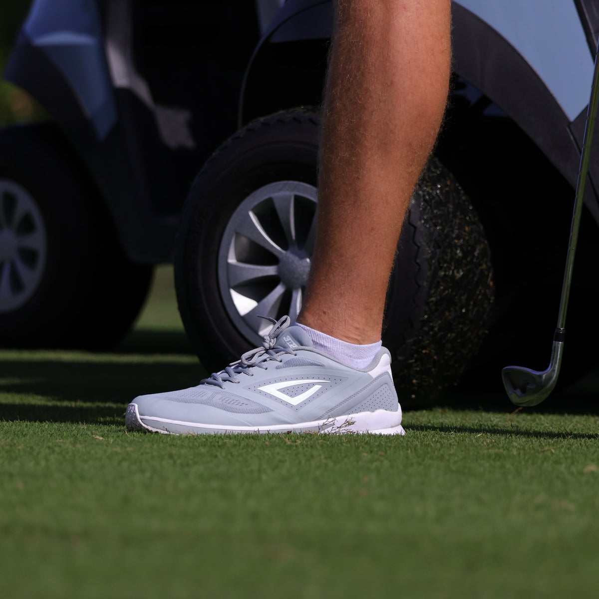 Person stepping out of a car with a golf club on a grassy area